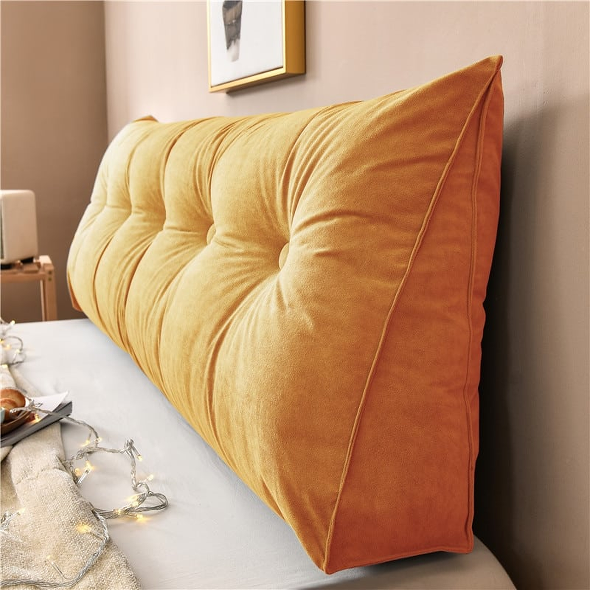 Coussin de chevet triangulaire orange terracotta posé en travers d'un lit, capitonnage et flanc visibles