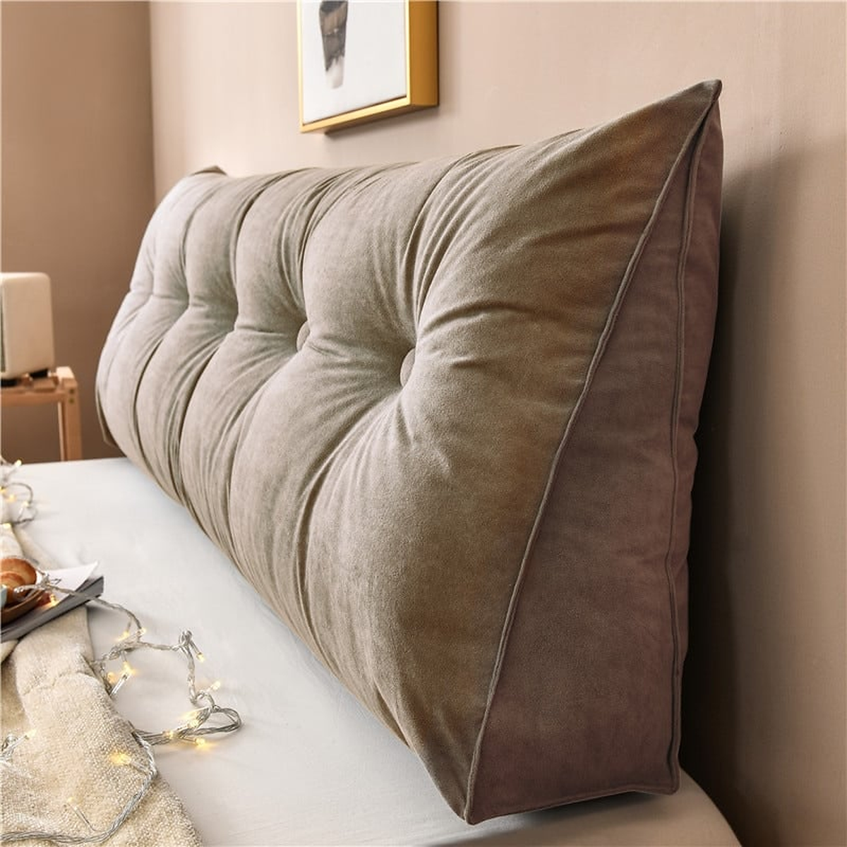 Coussin de chevet triangulaire brun clair posé en travers d'un lit, capitonnage et flanc visibles
