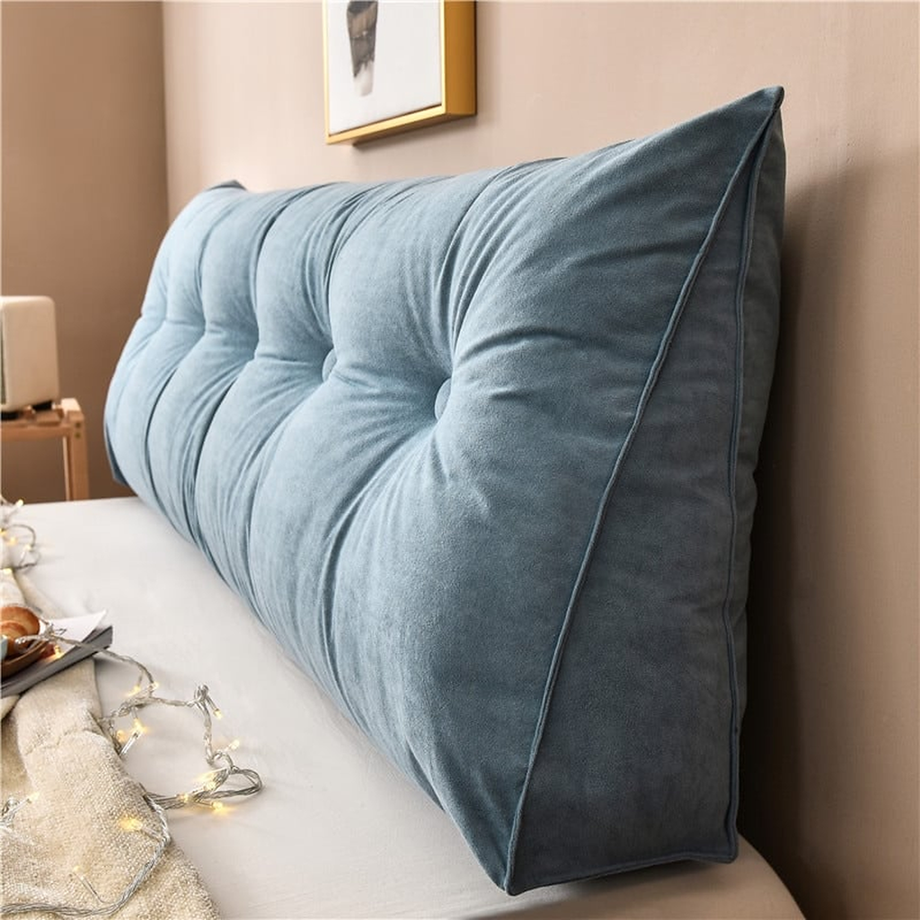 Coussin de chevet triangulaire bleu gris posé en travers d'un lit, capitonnage et flanc visibles