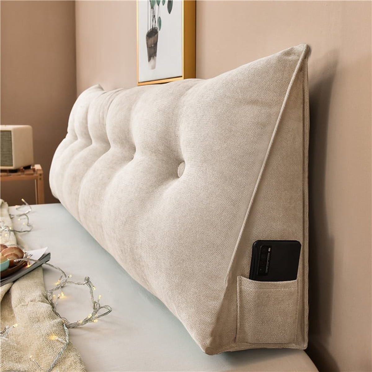 Coussin de chevet triangulaire beige sable posé en travers d'un lit, capitonnage et flanc visibles