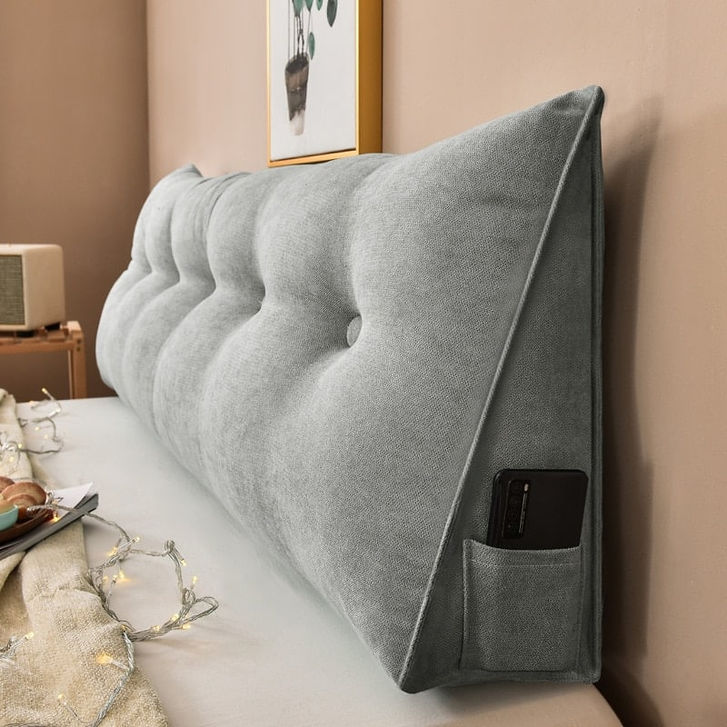 Coussin de chevet triangulaire gris clair posé en travers d'un lit, capitonnage et flanc visibles