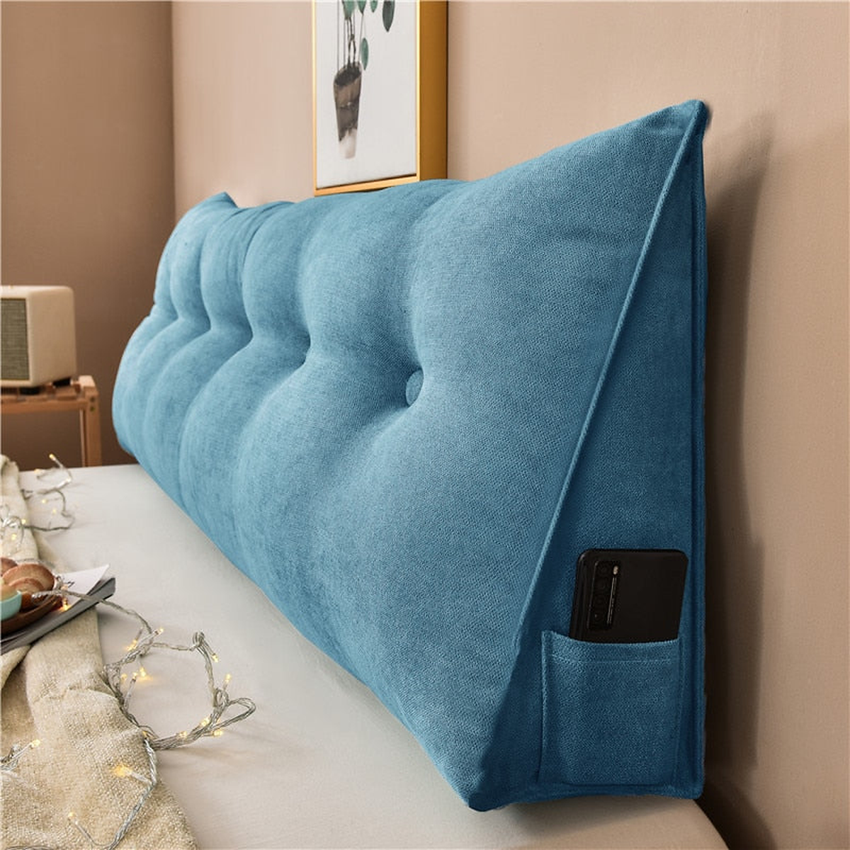 Coussin de chevet triangulaire bleu pétrole posé en travers d'un lit, capitonnage et flanc visibles
