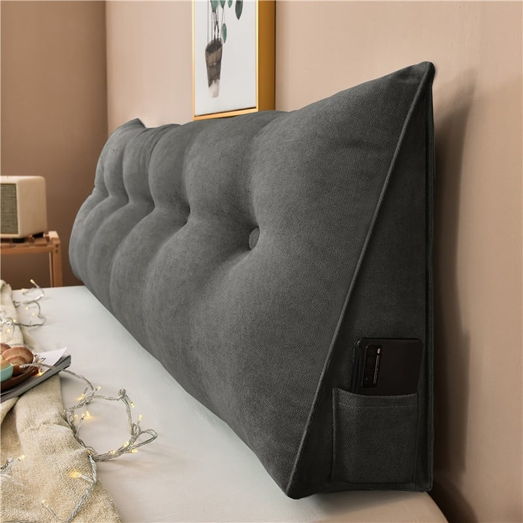 Coussin de chevet triangulaire gris anthracite posé en travers d'un lit, capitonnage et flanc visibles