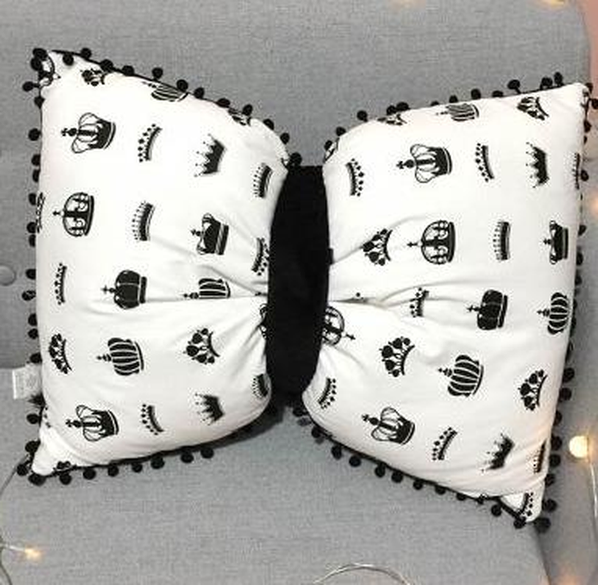 Coussin nœud papillon blanc à couronnes noires, posé sur un canapé gris