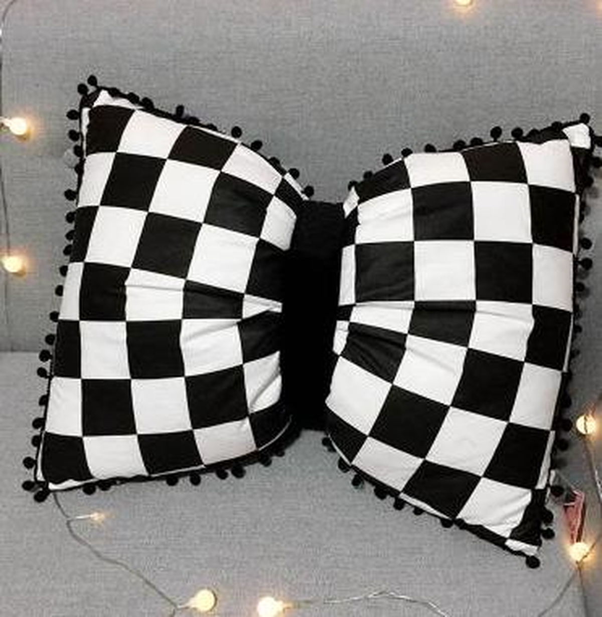 Coussin nœud papillon à damier noir, posé sur un canapé gris