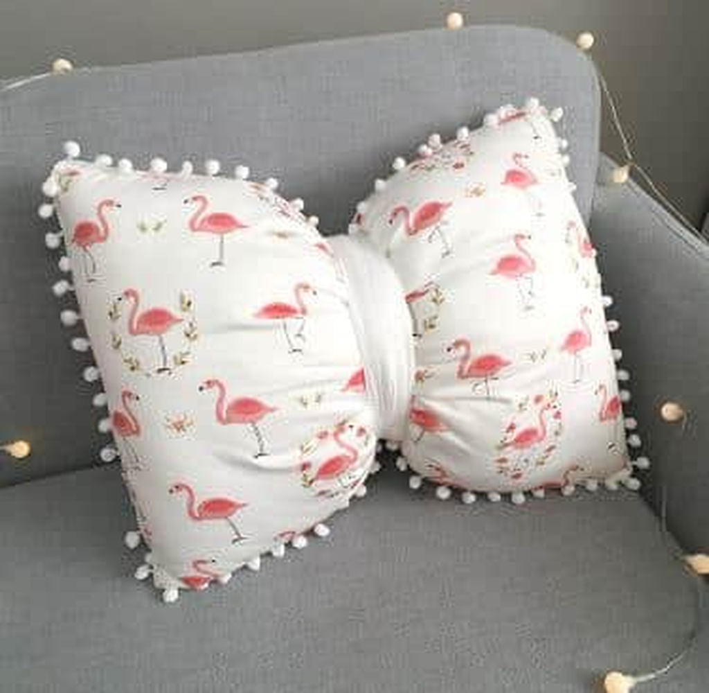 Coussin nœud papillon blanc à flamants roses, posé sur un canapé gris