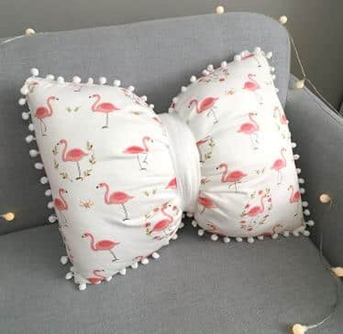 Coussin nœud papillon blanc à flamants roses, posé sur un canapé gris