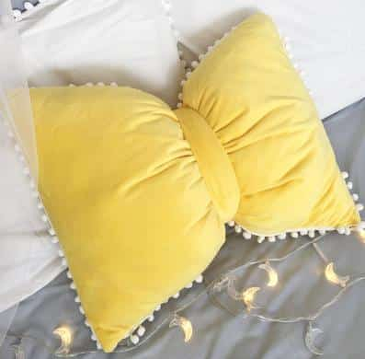 Coussin nœud papillon jaune, posé sur un canapé gris
