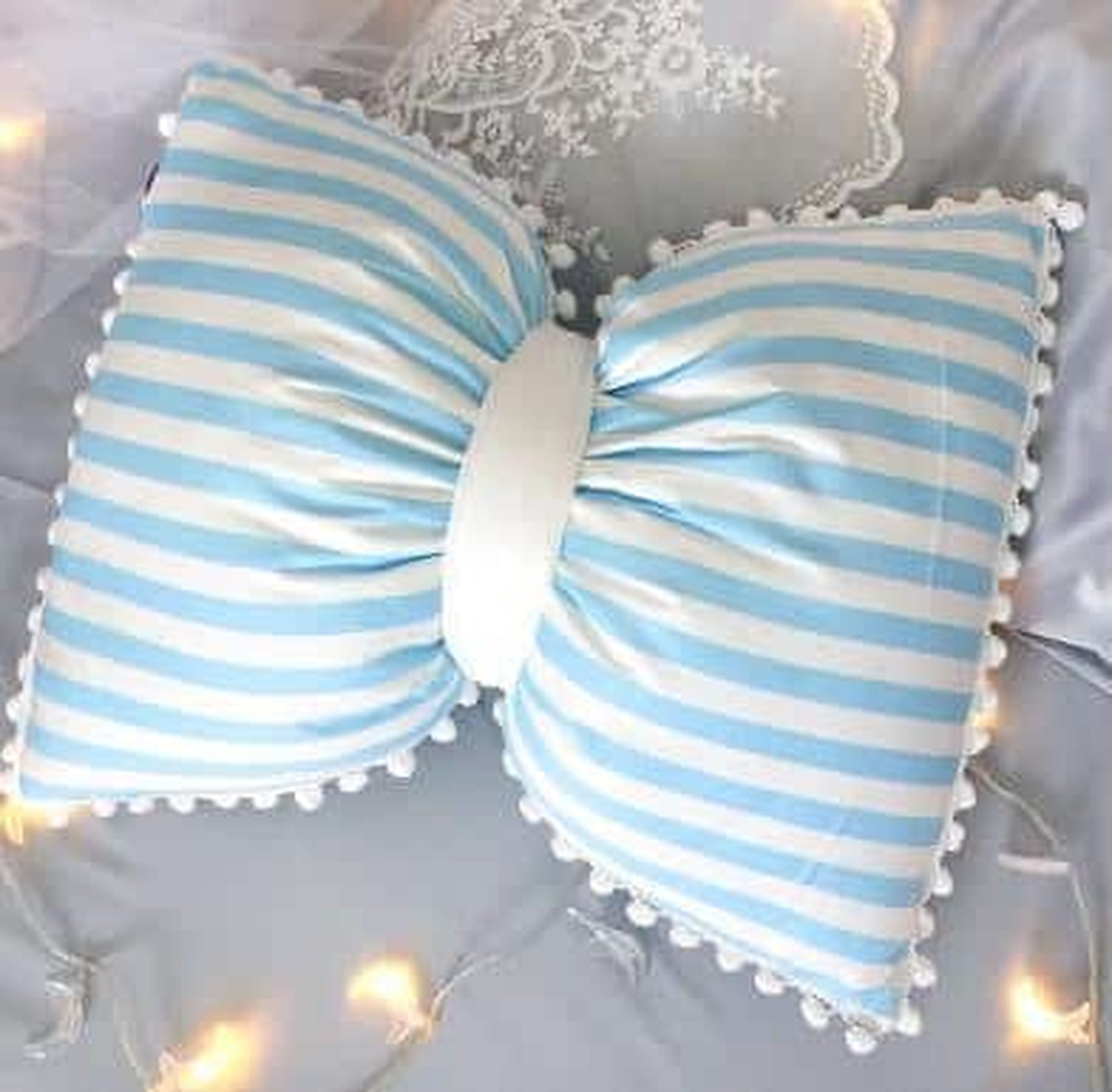 Coussin nœud papillon à rayures bleu ciel, posé sur un canapé gris