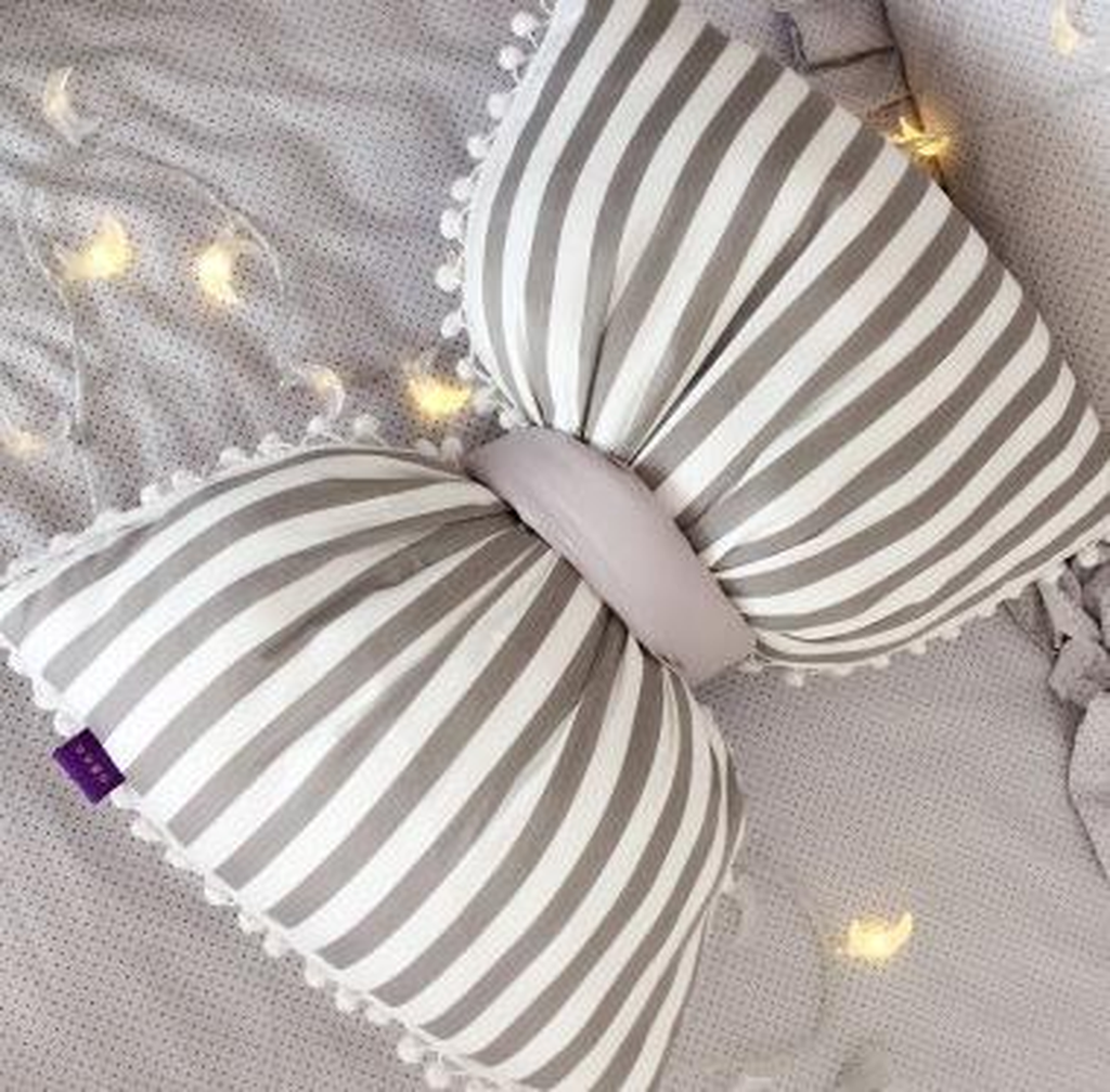 Coussin nœud papillon blanc à rayures grises, posé sur un canapé gris