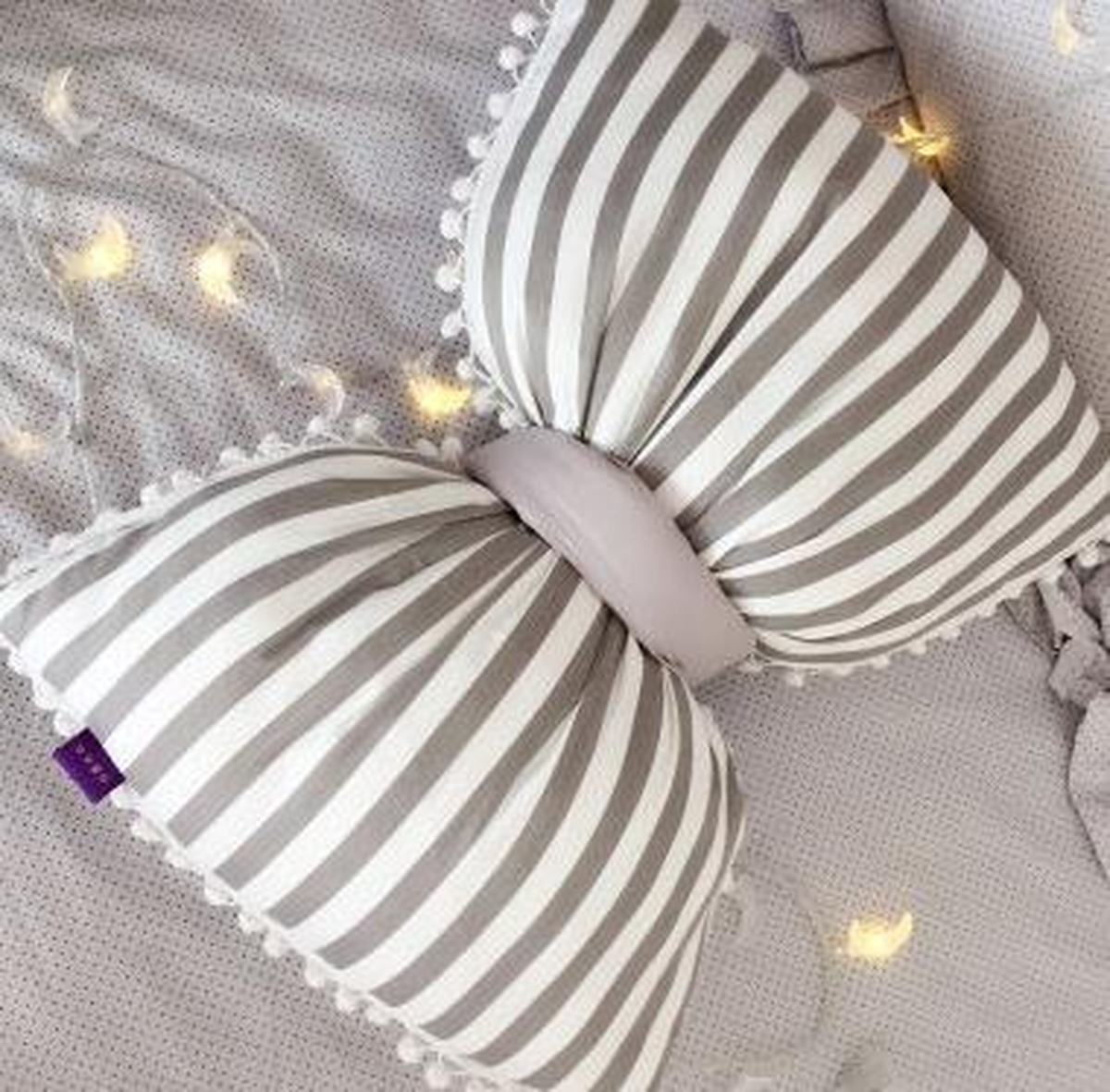 Coussin nœud papillon blanc à rayures grises, posé sur un canapé gris