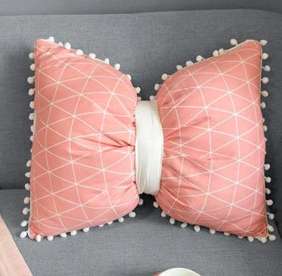 Coussin nœud papillon rose à motif géométrique, posé sur un canapé gris