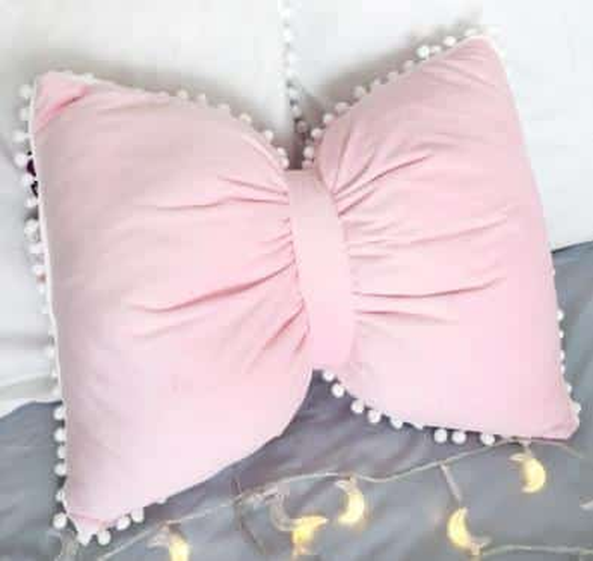 Coussin nœud papillon rose poudré, posé sur un canapé gris