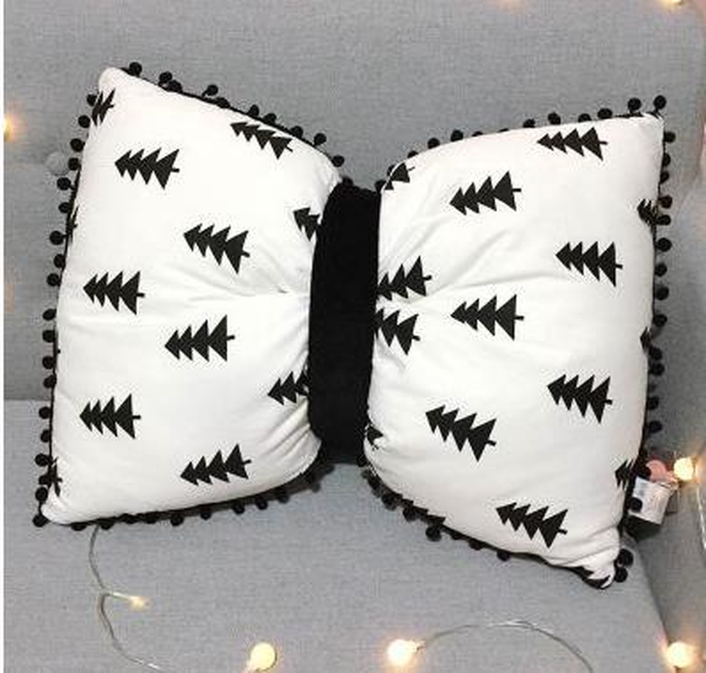 Coussin nœud papillon blanc à sapins noirs, posé sur un canapé gris