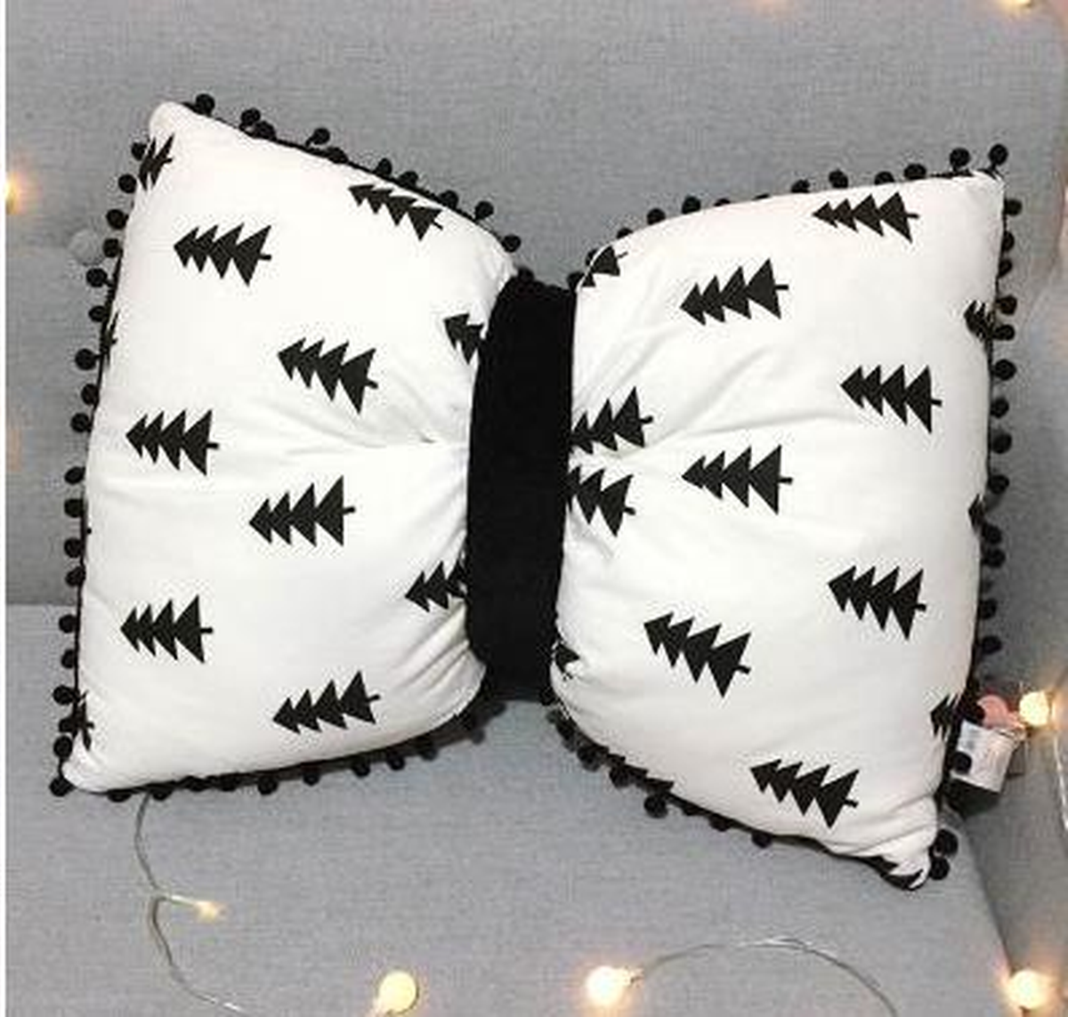 Coussin nœud papillon blanc à sapins noirs, posé sur un canapé gris