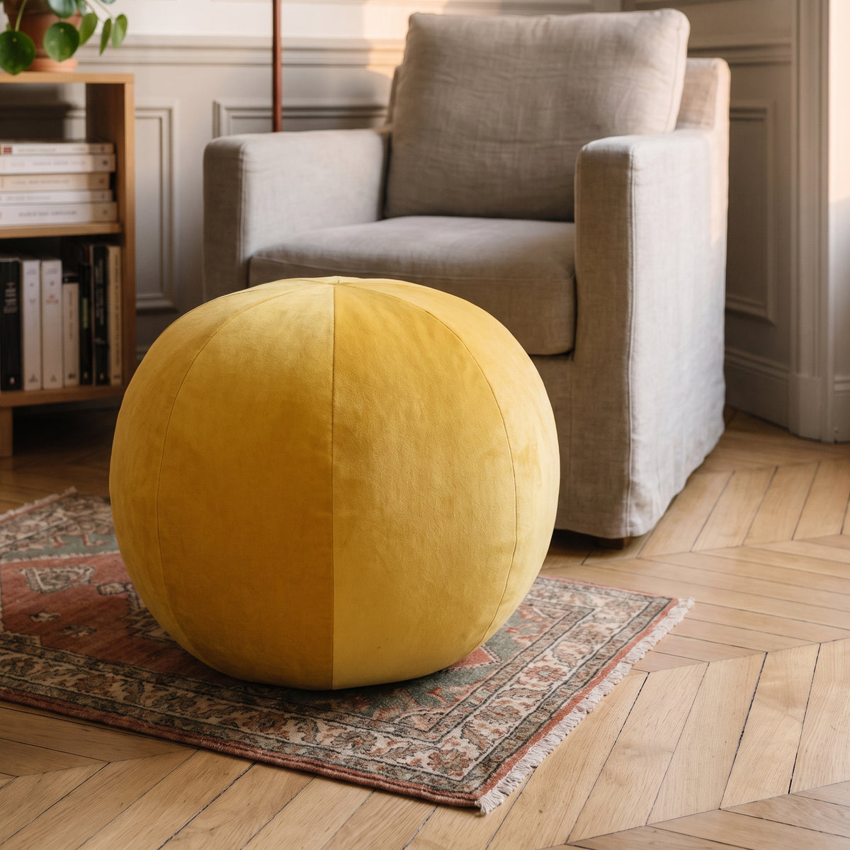 Coussin rond nordique en velours jaune, posé au sol près du fauteuil de lecture Image