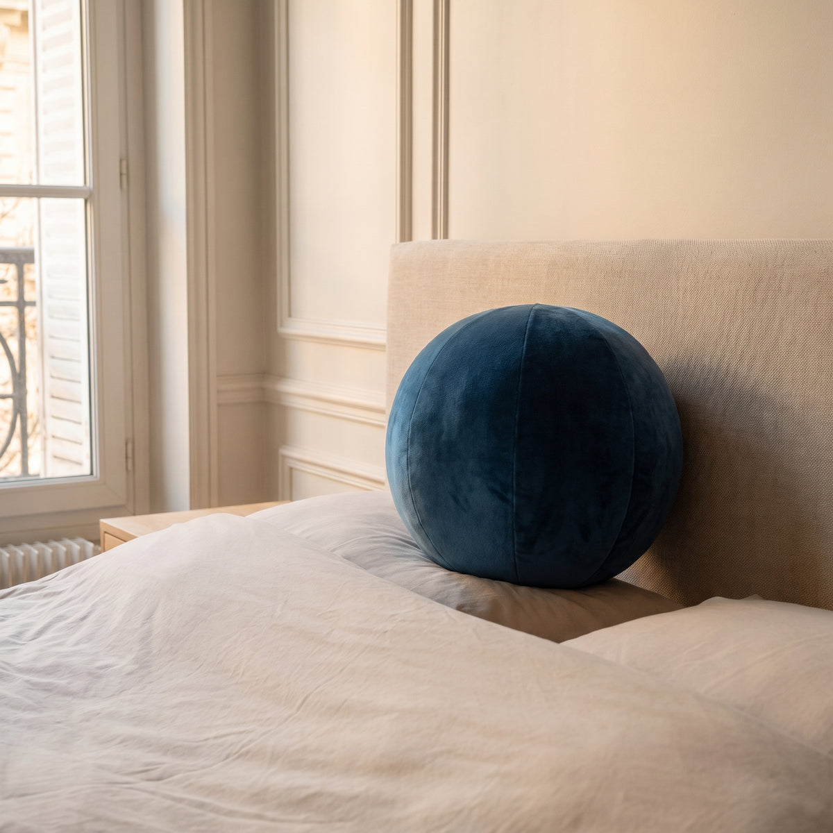Coussin rond nordique en velours bleu foncé, posé sur le lit contre la tête de lit Image