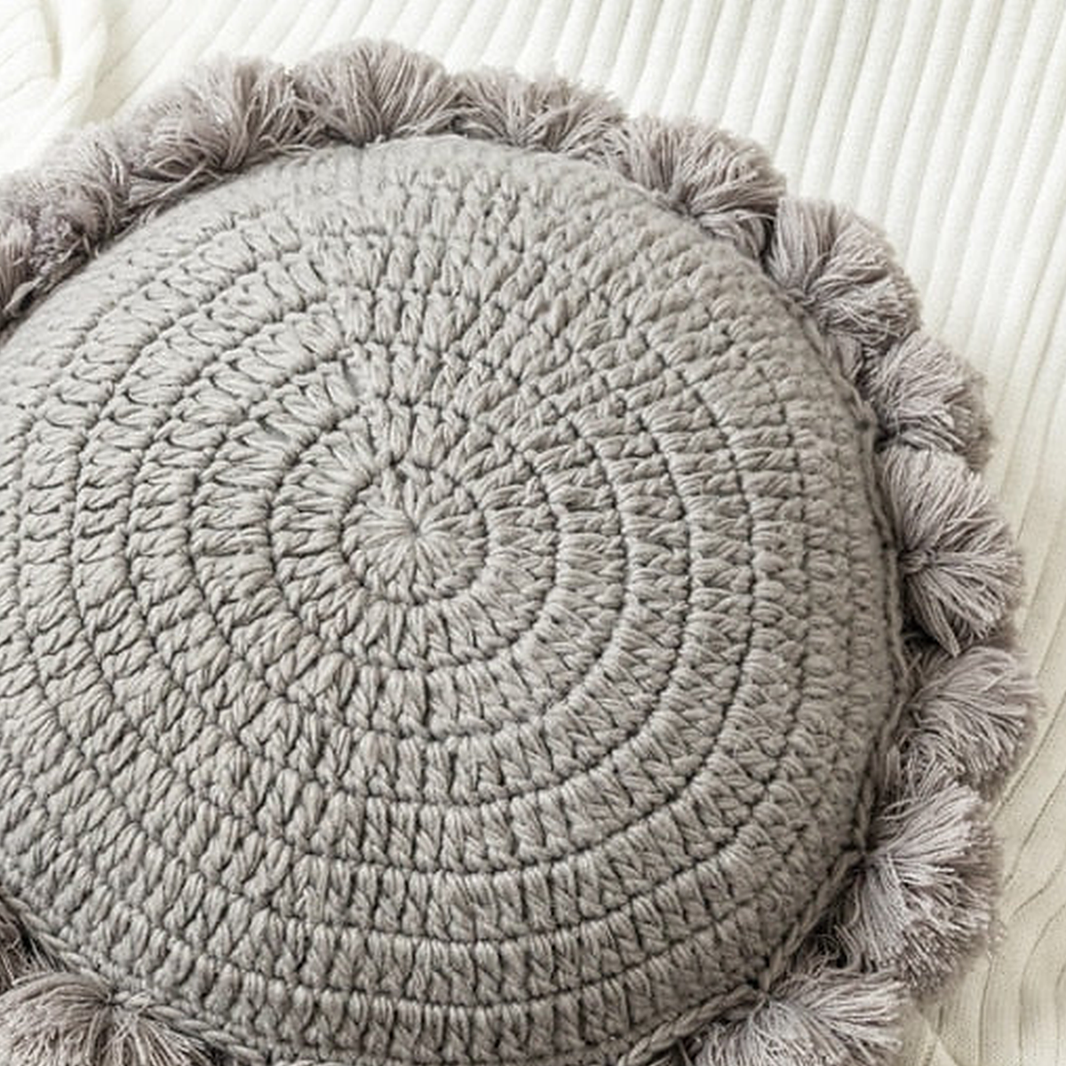 Gros plan sur la maille tricotée en spirale et la bordure de pompons du coussin rond gris