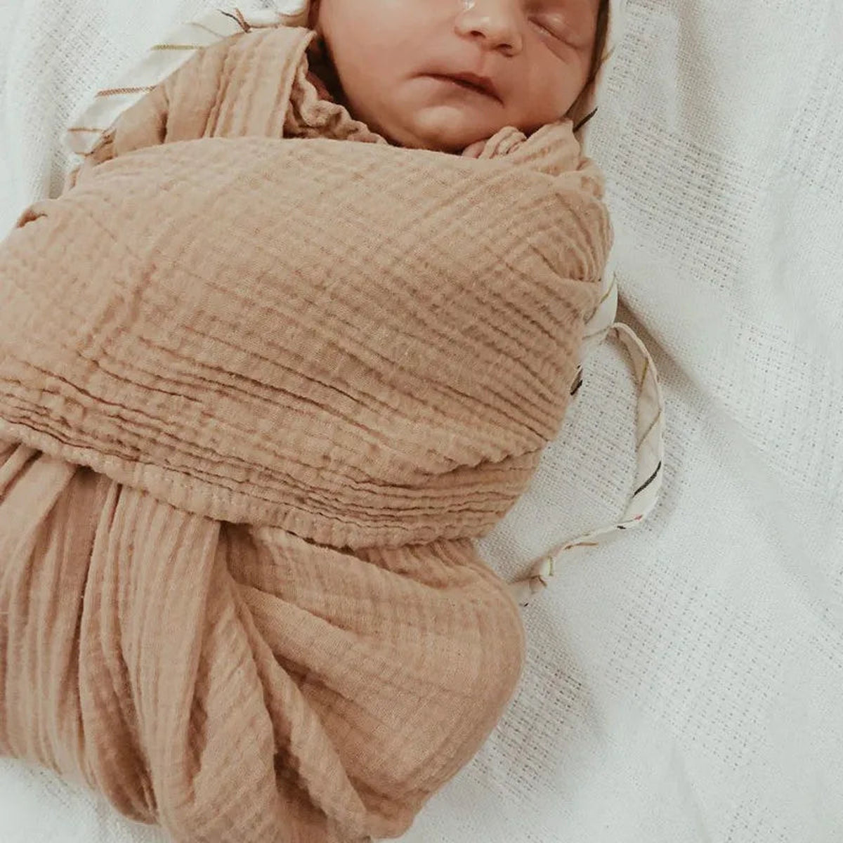Bébé enveloppé dans la couverture en mousseline marron, visage et mains dégagés