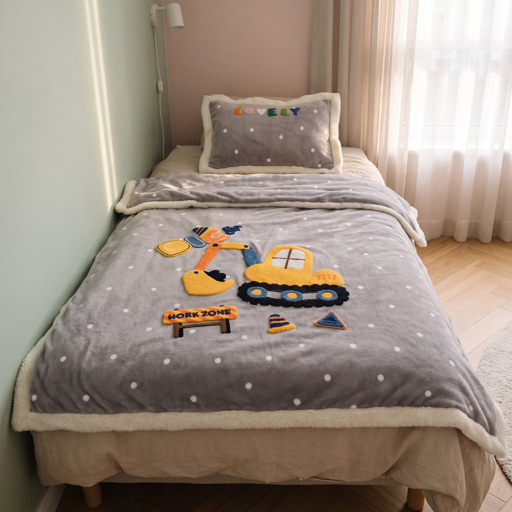 Couverture bébé grise à motif chantier posée sur un lit d’enfant