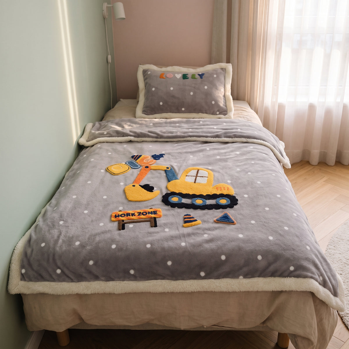 Couverture bébé grise à motif chantier posée sur un lit d’enfant