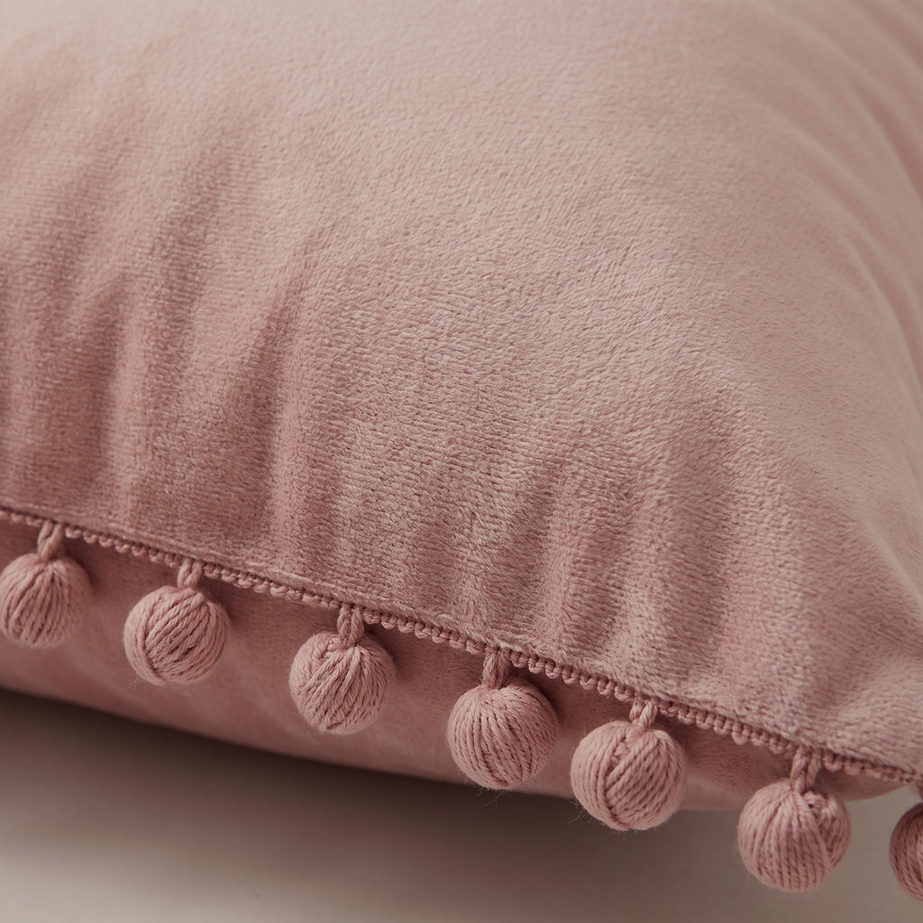 Détail du velours et de la frange de pompons de la housse de coussin rose