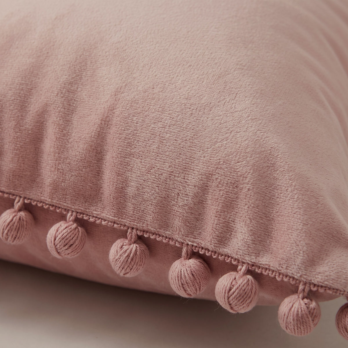 Détail du velours et de la frange de pompons de la housse de coussin rose
