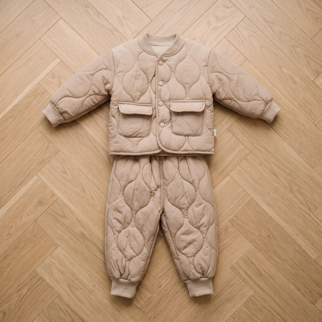 Ensemble bébé matelassé beige, veste et pantalon posés à plat sur un parquet clair