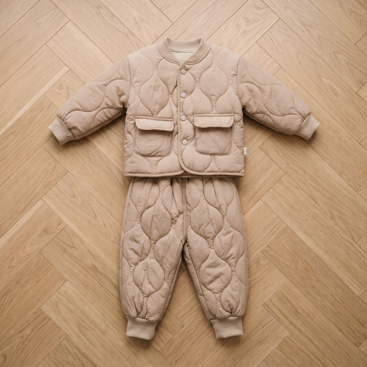 Ensemble bébé matelassé beige, veste et pantalon posés à plat sur un parquet clair