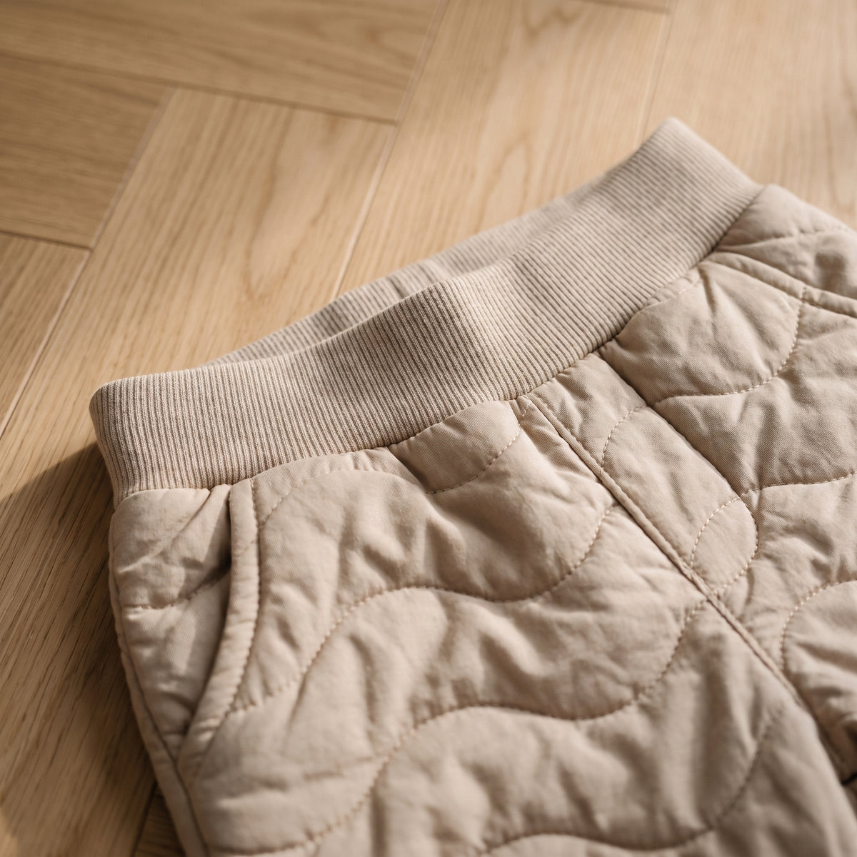 Gros plan sur la ceinture côtelée élastiquée du pantalon matelassé beige