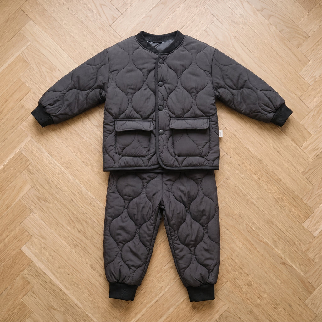 Ensemble bébé matelassé noir, veste et pantalon posés à plat sur un parquet clair