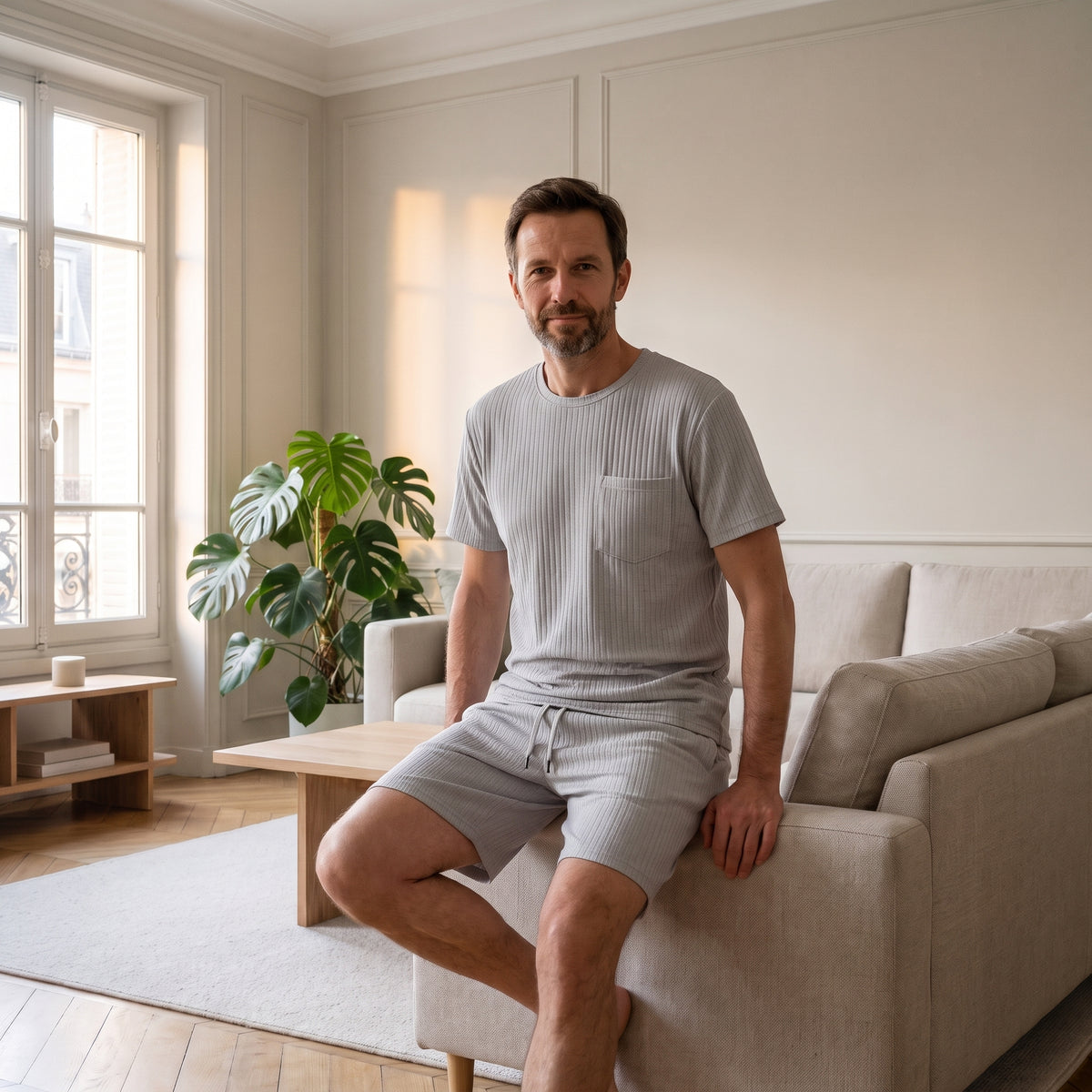 Homme assis au bord du canapé en ensemble t-shirt et short gris en tissu plissé Image