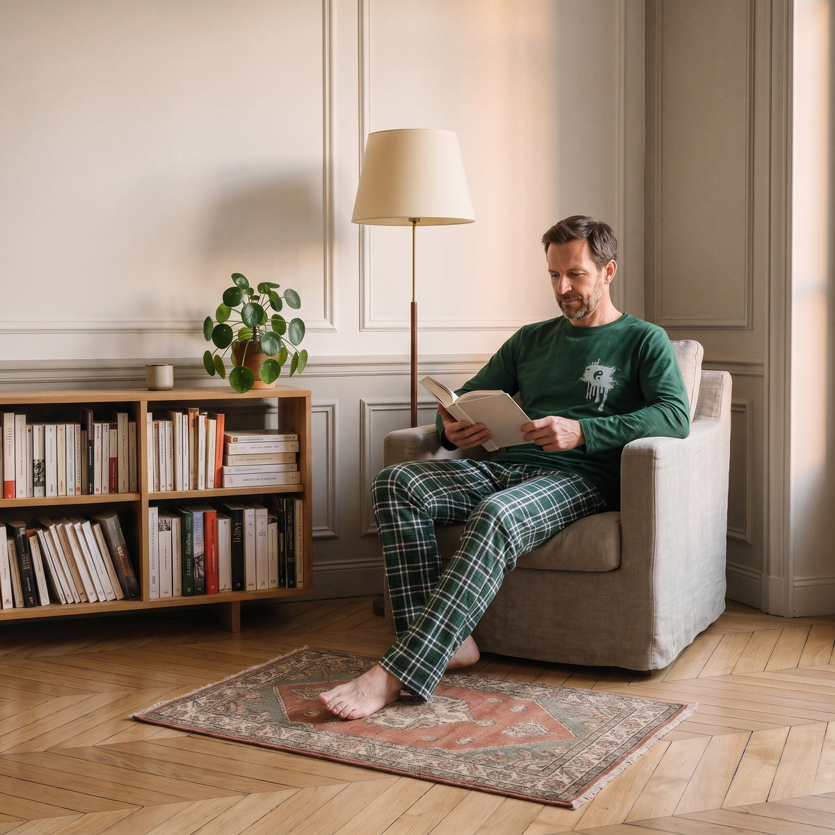 Coin lecture d'un appartement, un homme en ensemble pyjama assis dans le fauteuil, un livre ouvert Image