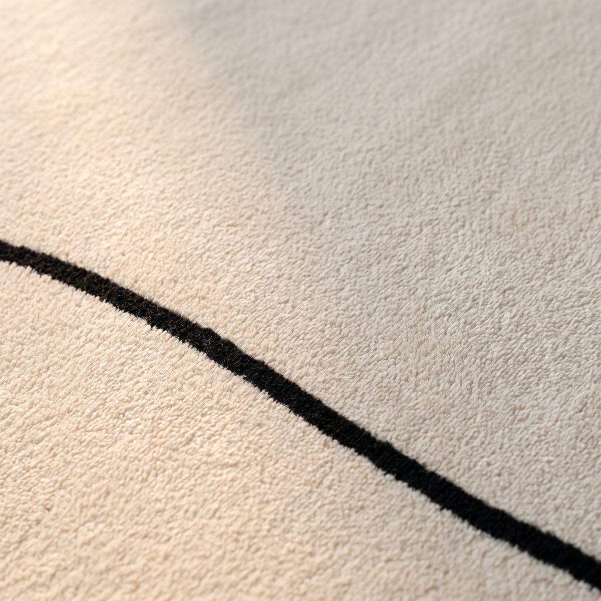 Surface veloutée écru du tapis vue de très près, traversée par le liseré noir plat