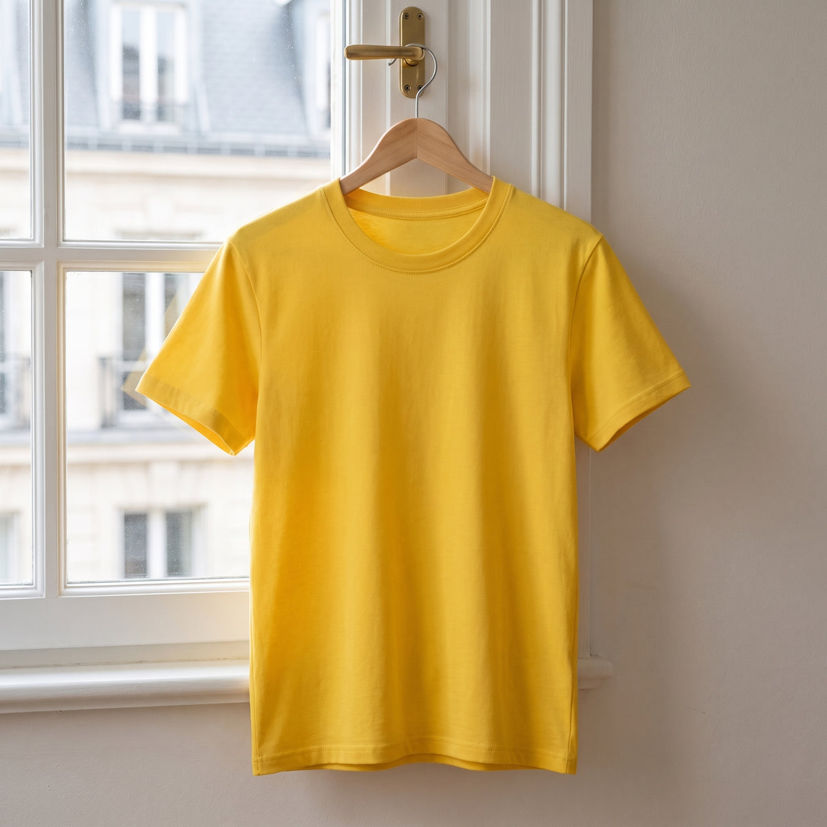 T-shirt cocooning jaune suspendu à un cintre devant la fenêtre