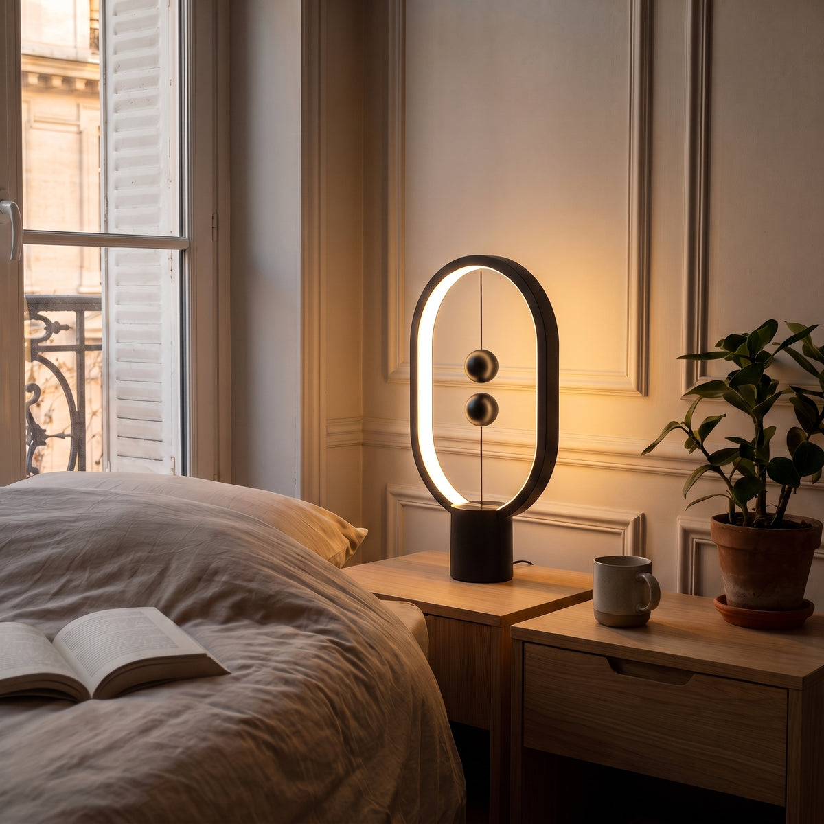 Lampe de chevet ovale en métal noir à billes magnétiques, allumée sur une table de chevet en bois clair