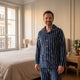 Homme debout en pyjama de flanelle bleu marine à rayures blanches, dans une chambre