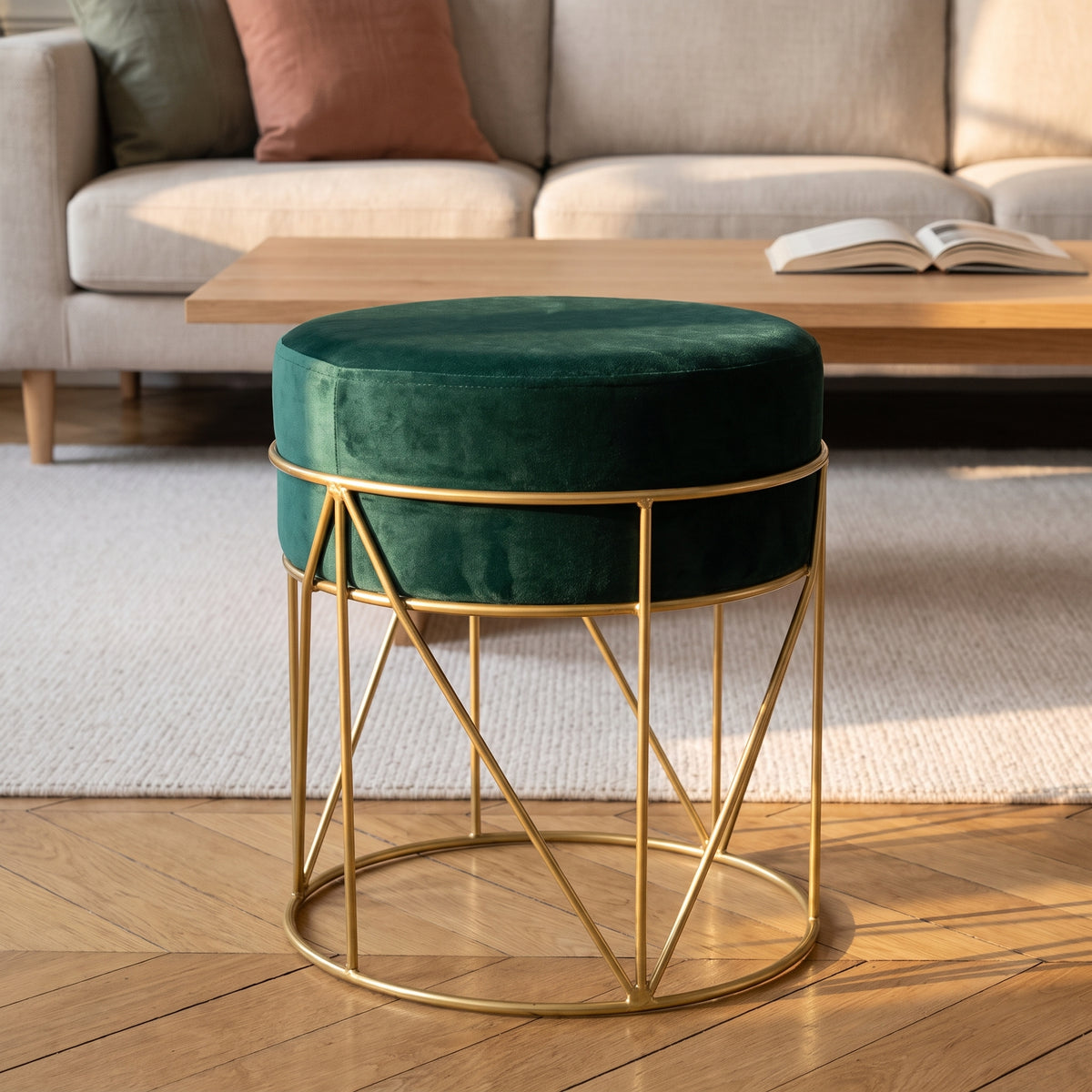 Pouf rond en velours vert sapin sur piètement doré, devant un canapé beige