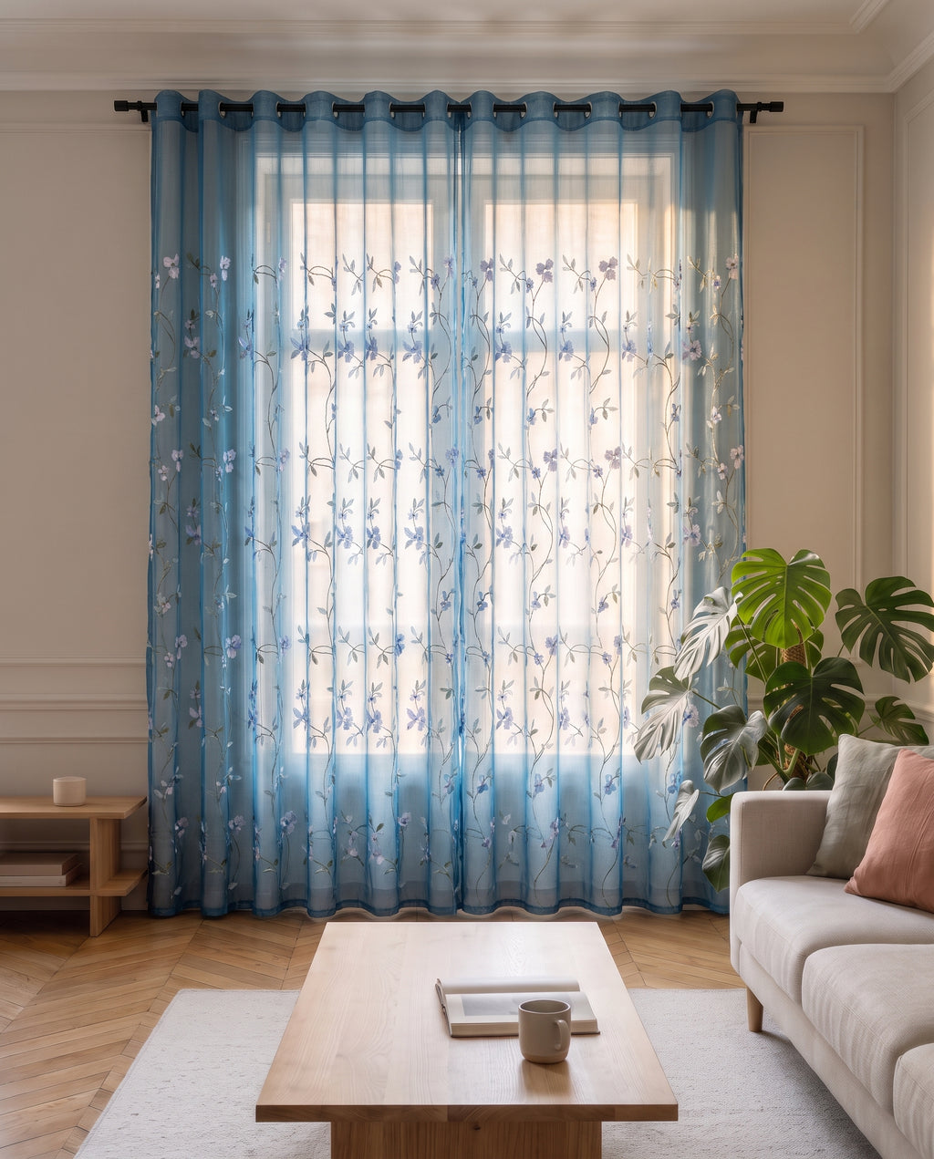 Voilage en tulle brodé bleu tiré devant la fenêtre d'un salon, du plafond jusqu'au parquet