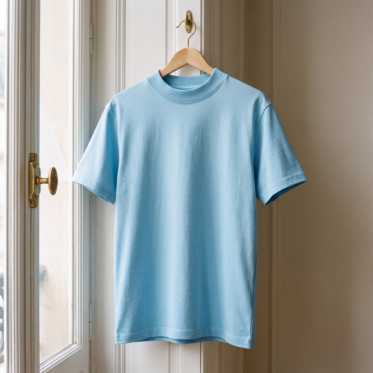 T-shirt cocooning bleu clair suspendu à un cintre devant la fenêtre