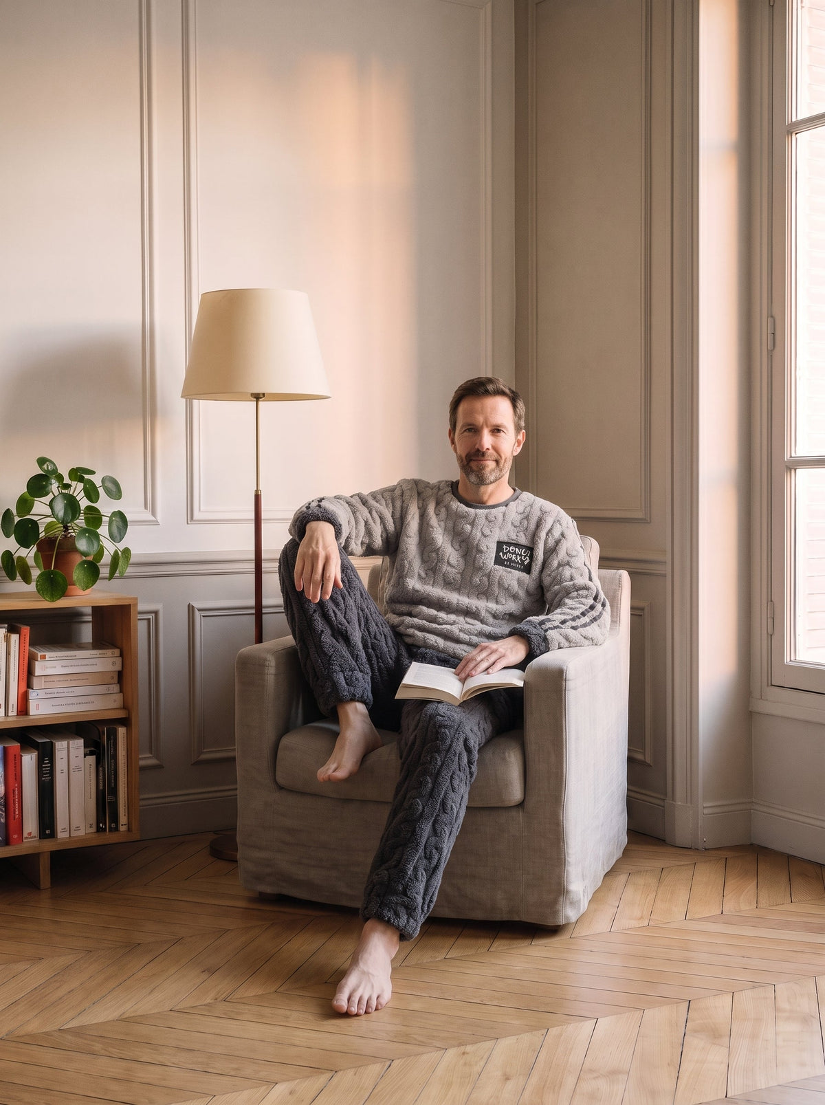 Pyjama polaire gris clair et anthracite porte assis dans le fauteuil de lecture, ecusson Donut Worry sur la poitrine.
