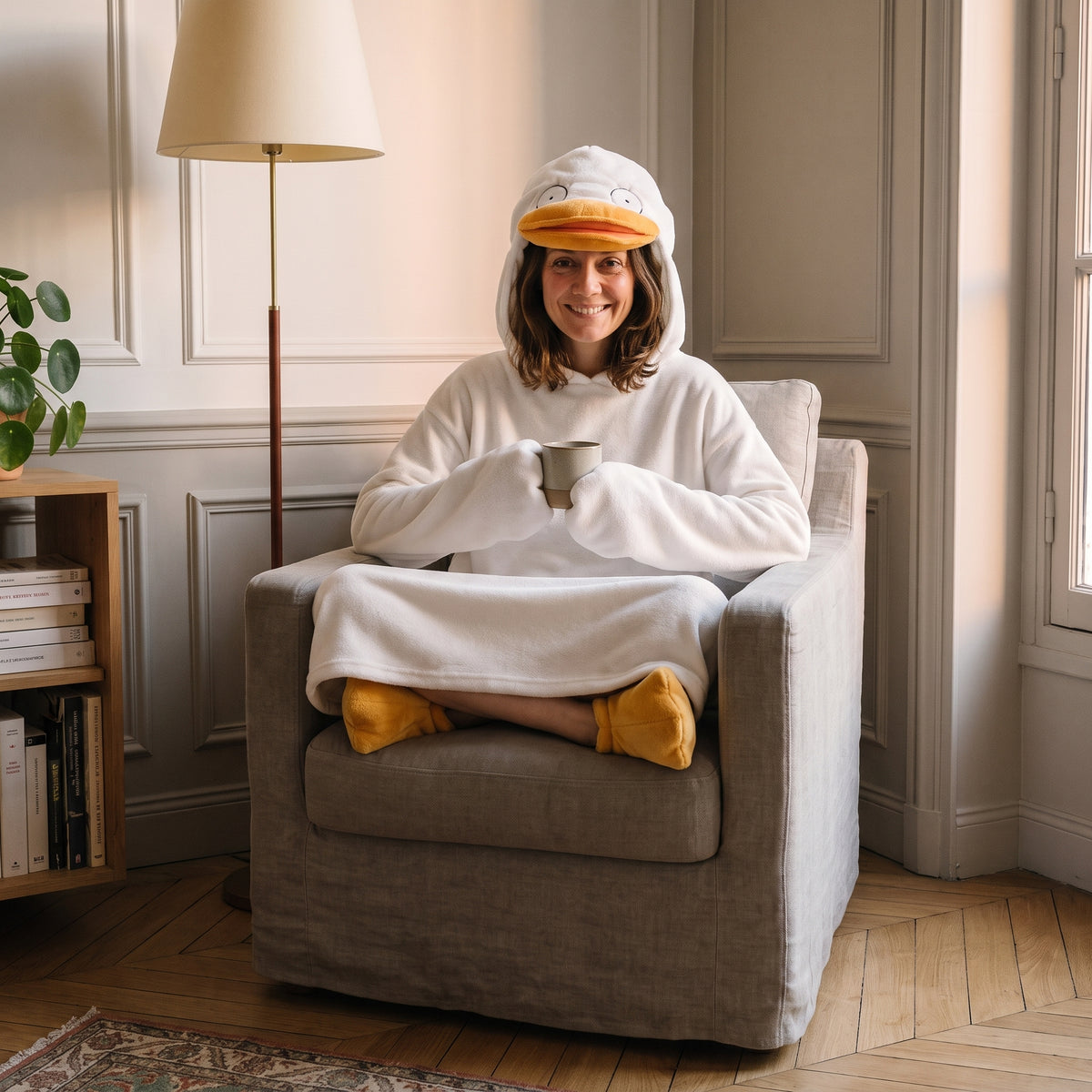 Pyjama canard porté en tailleur dans un fauteuil de lecture, une tasse tenue entre les deux manches en aile