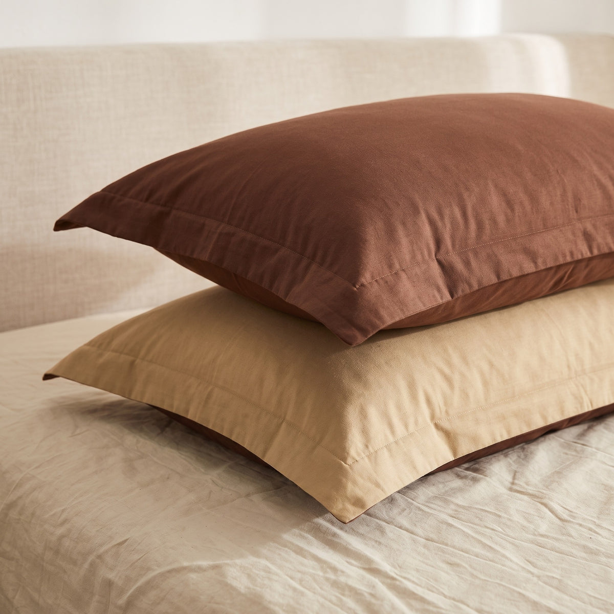 Deux taies d oreiller empilees, une marron et une beige, leur bord plat visible sur tout le pourtour