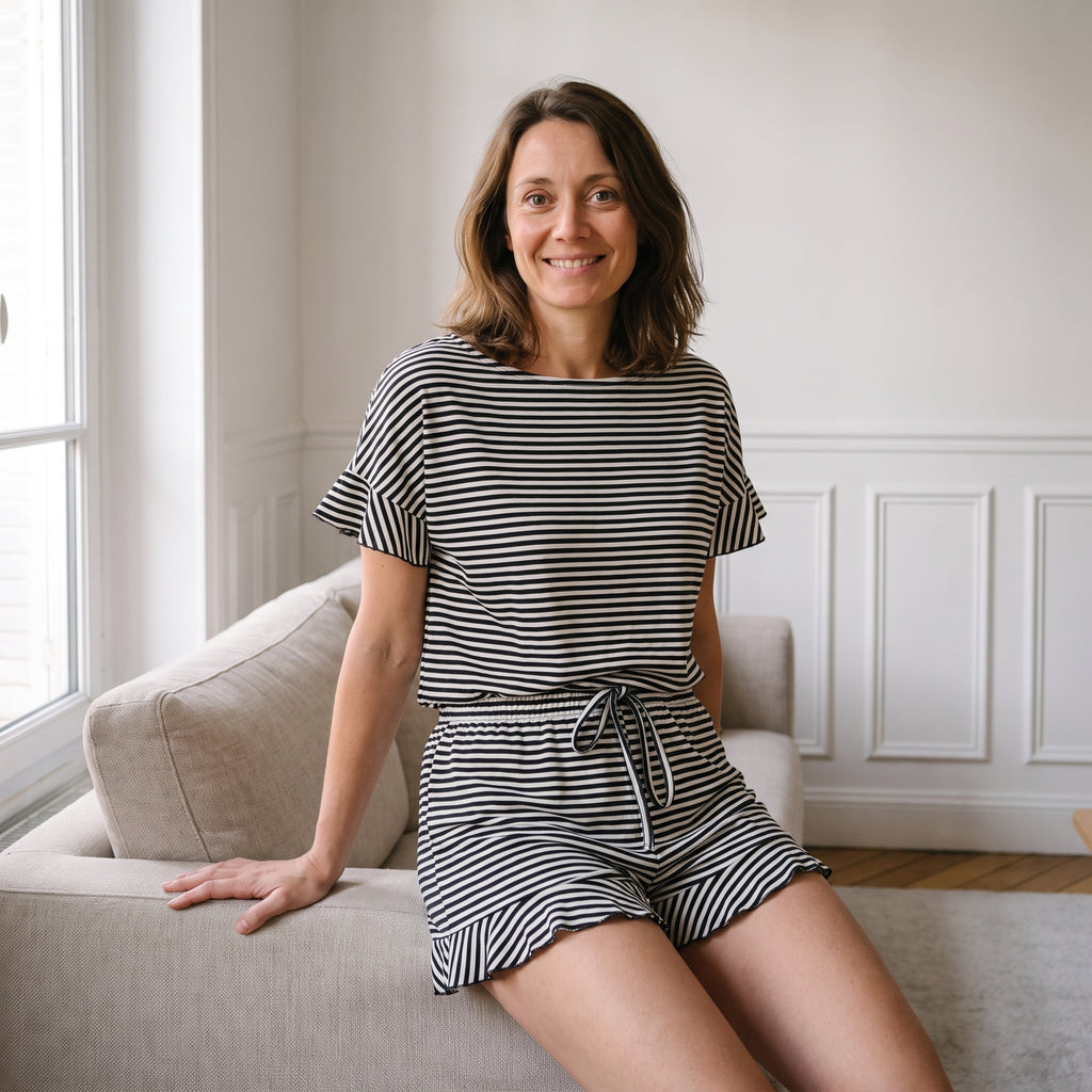 Femme assise sur un canapé en ensemble pyjama d'été à rayures noires