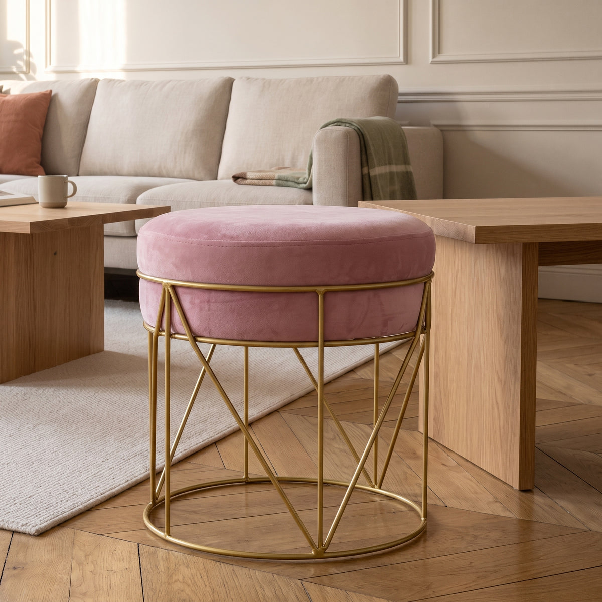 Pouf rond en velours rose poudré sur piètement doré, près d'une table basse en chêne