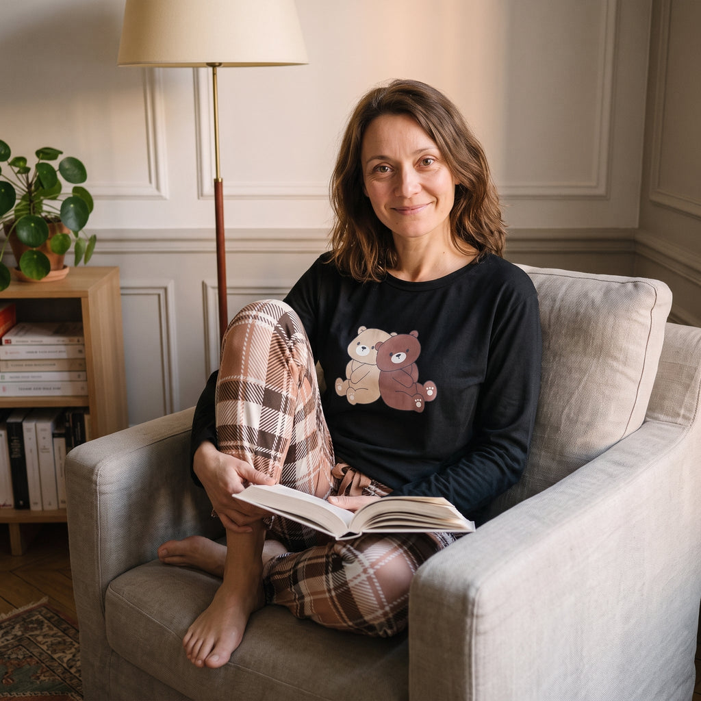 Femme lisant dans son fauteuil en pyjama noir imprime ours, jambes repliees sous elle