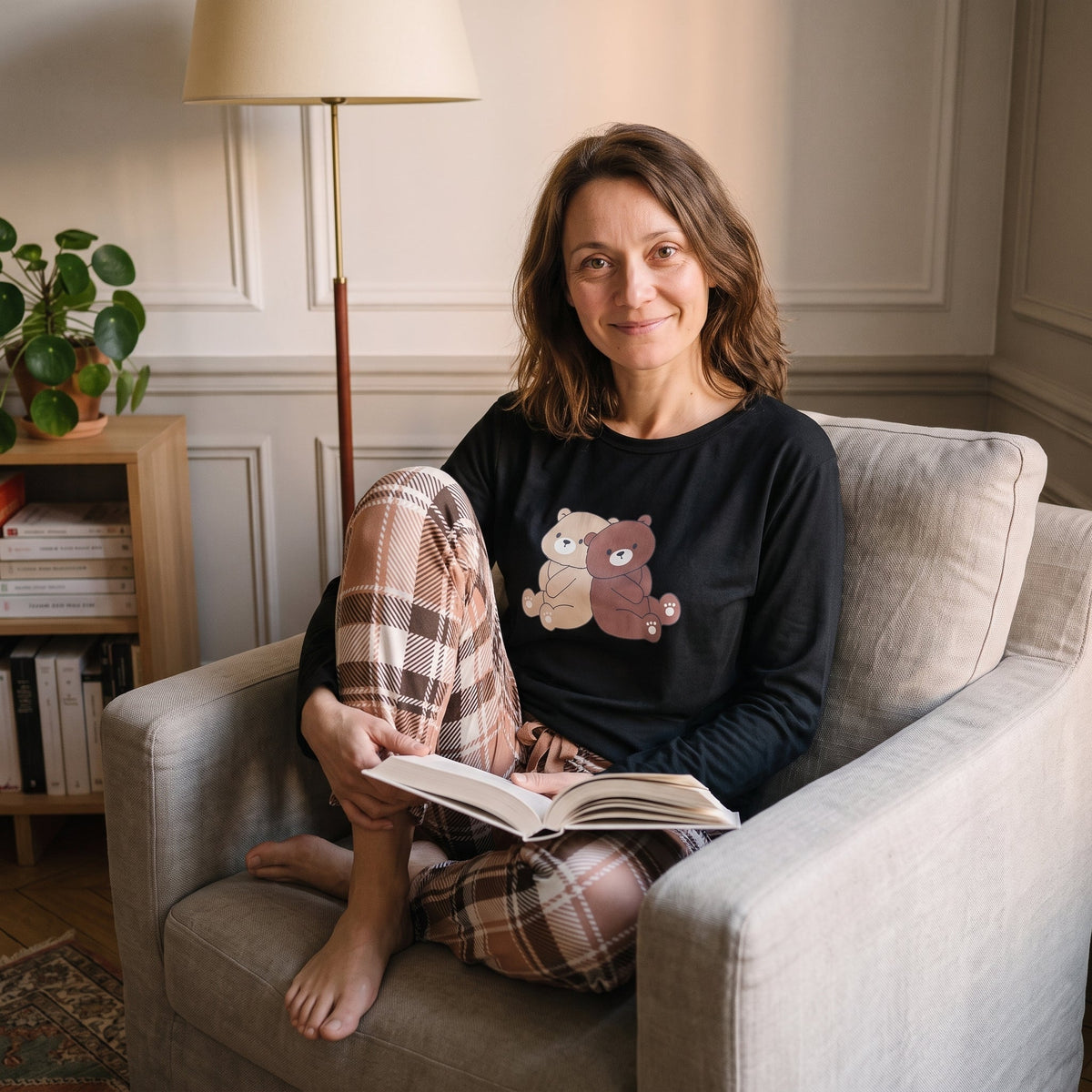 Femme lisant dans son fauteuil en pyjama noir imprime ours, jambes repliees sous elle