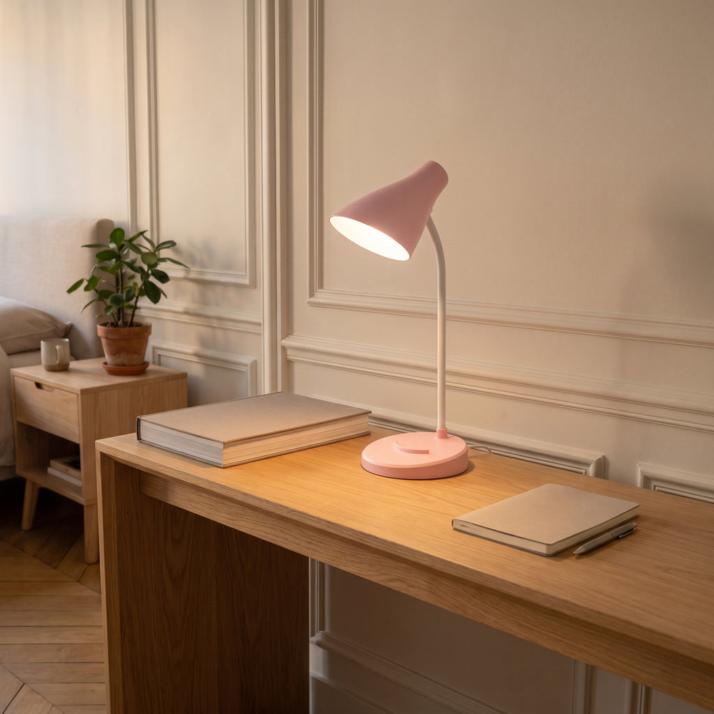 La lampe rose allumée au bord d'une console en chêne, un gros livre relié à sa gauche et un carnet à sa droite, la lumière étalée sur le bois.
