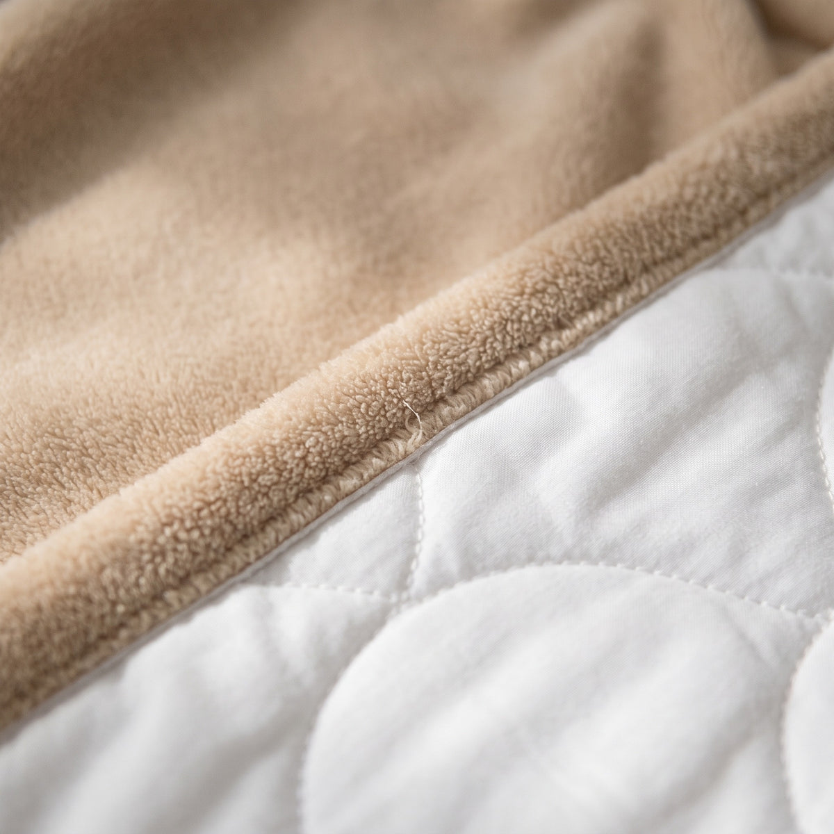 Gros plan sur le bord d un pan : la polaire beige a poil ras rabattue en bande le long du coton matelasse blanc, avec la surpiqure arrondie de la doublure