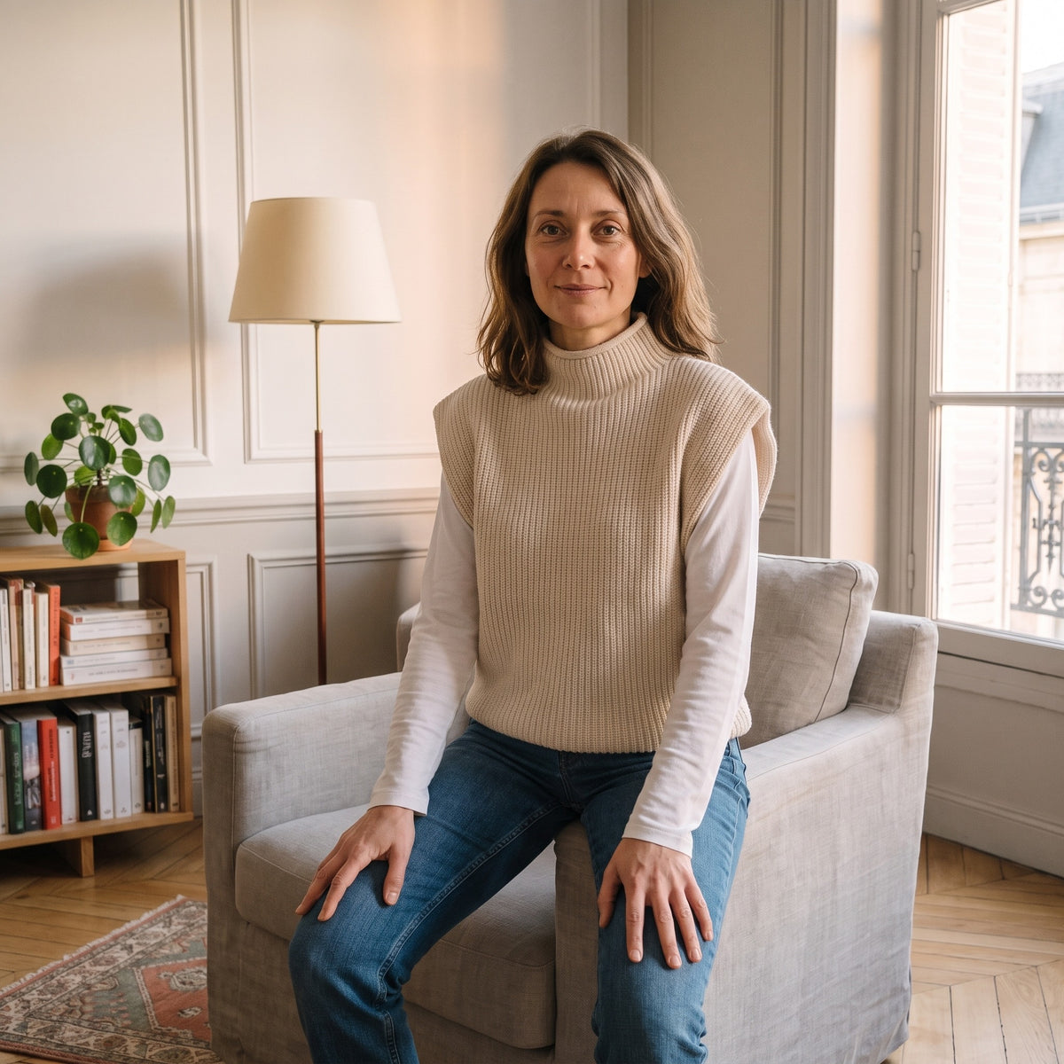Le pull beige enfilé par-dessus un tee-shirt blanc à manches longues, assise sur l'accoudoir d'un fauteuil